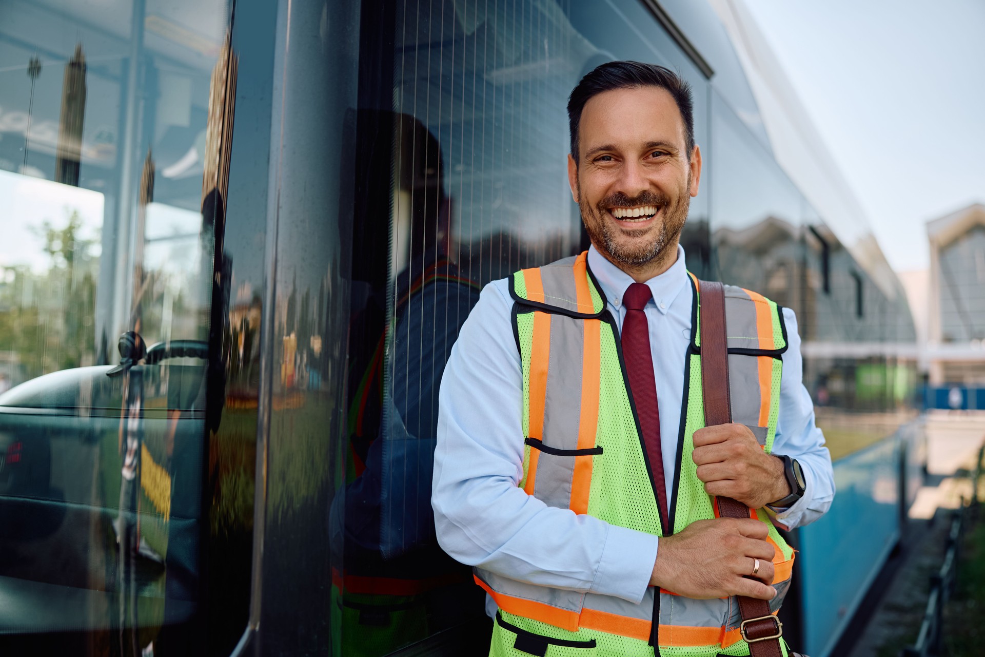 Happy driver standing next to a city bus and looking at camera.